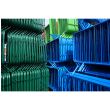 Tightly stacked green and blue barriers, with visible diagonal support legs in storage yard.