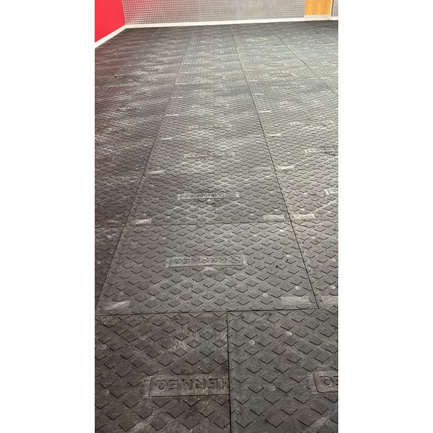 Wide view of gym floor fitted with interlocked black floor protection mats, displaying HERMEQ logo and non-slip diamond texture.