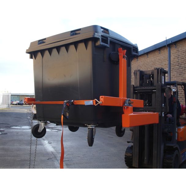 Industrial forklift wheelie bin tipper attachment transporting large black waste bin with secure chain and strap system.