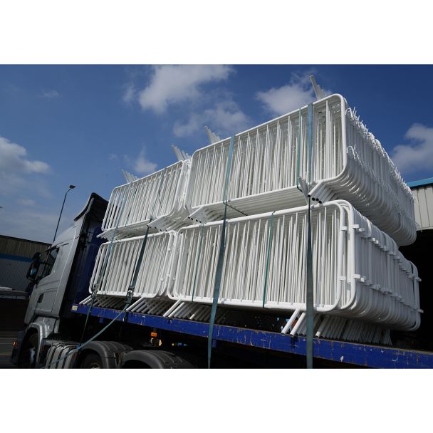 White barriers loaded onto a flatbed truck, stacked and secured with straps, ready for transport under a blue sky.